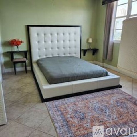 A bed with a white headboard and grey bedspread is in a room with a patterned rug.