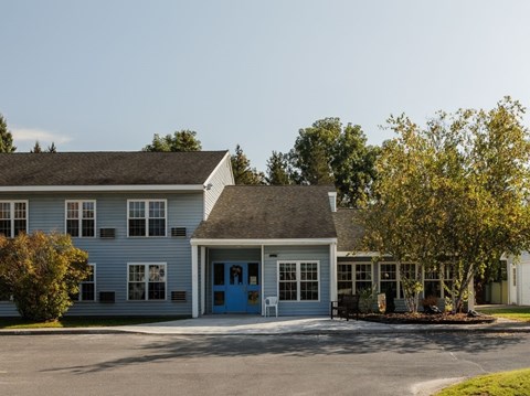A small building with a blue door and windows surrounded by trees.