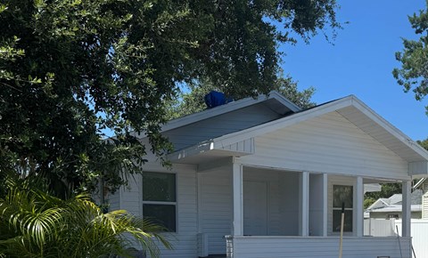 A house with a white siding and a blue roof is surrounded by trees.