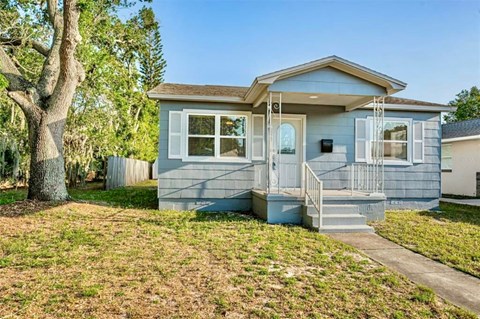 A small blue house with a tree in front of it.