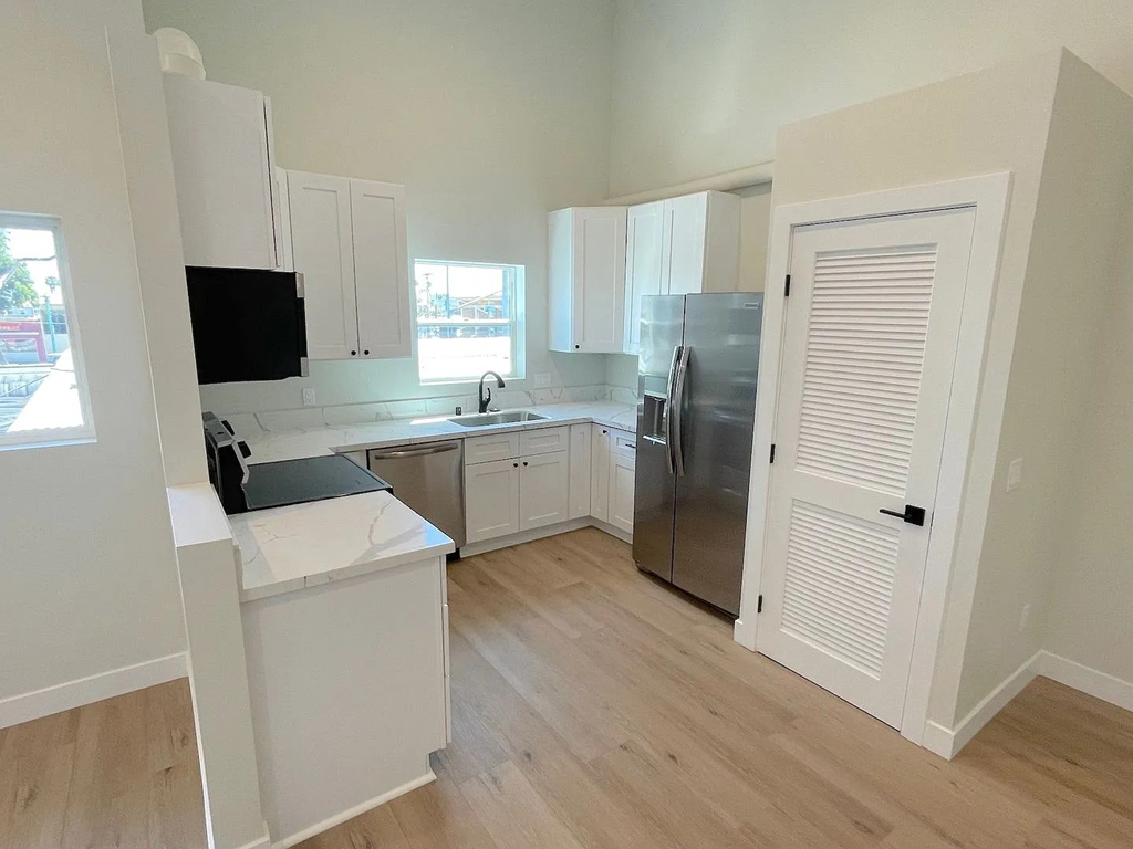 A kitchen with white cabinets and a black fridge.