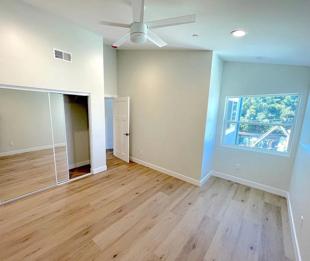 A room with a ceiling fan and a window showing a view of trees.