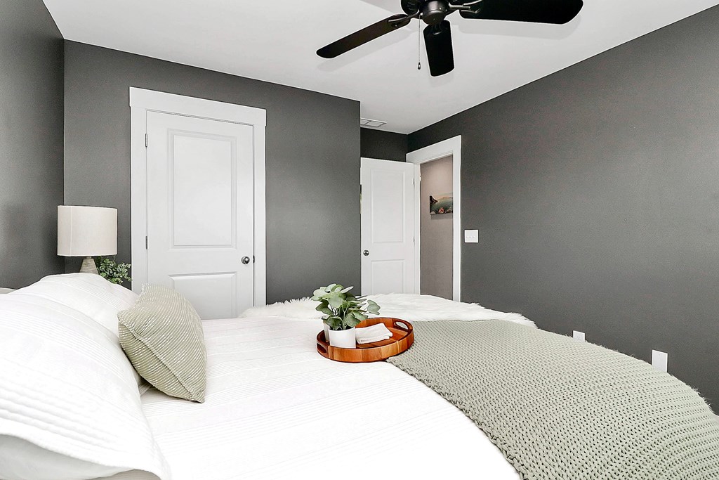 A bedroom with a bed, pillows, a ceiling fan, and a small potted plant.