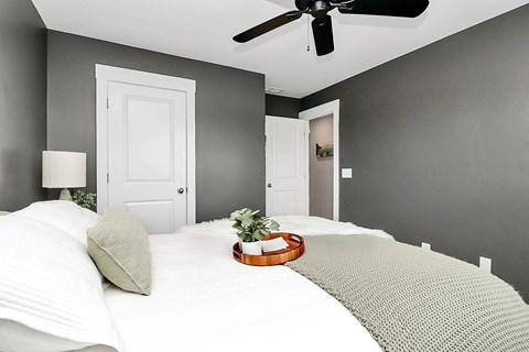 A bedroom with a bed, pillows, a ceiling fan, and a small potted plant.
