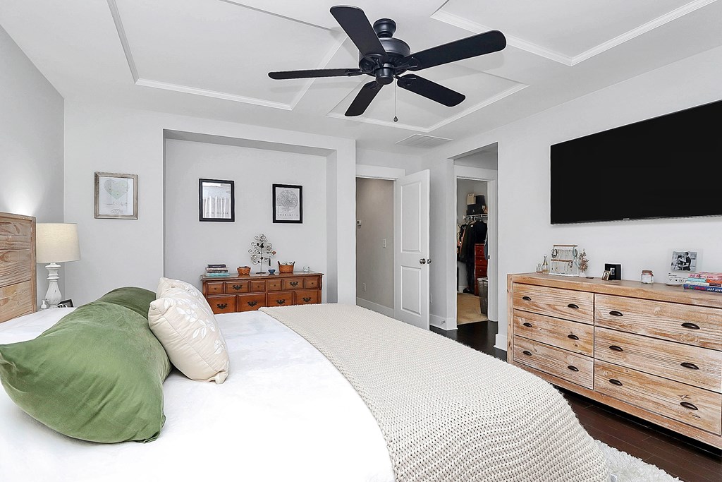 A bedroom with a bed, a ceiling fan, and a dresser.