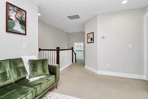 A living room with a green couch and a painting of a bride on the wall.