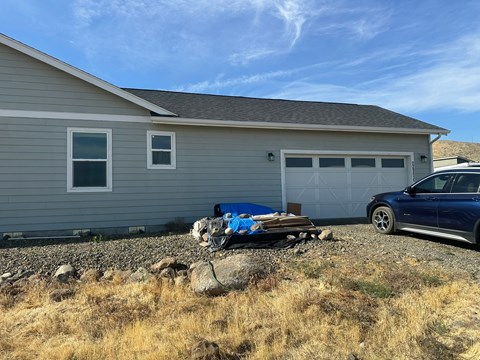 A blue car is parked in front of a grey house.