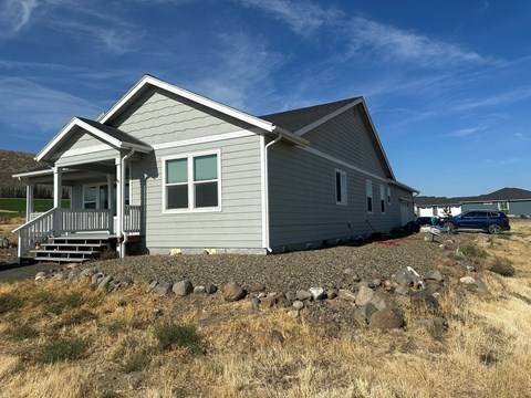 A house with a grey siding and a porch is surrounded by rocks and grass.