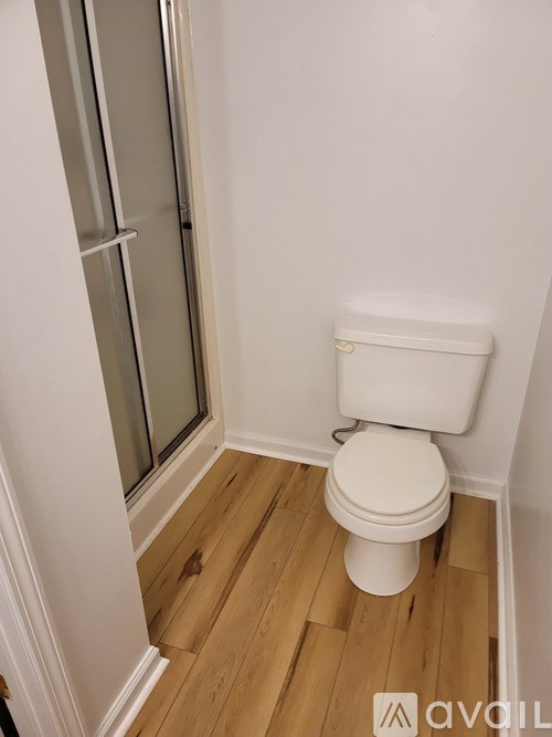 A white toilet in a small bathroom with wood flooring and a glass shower door.