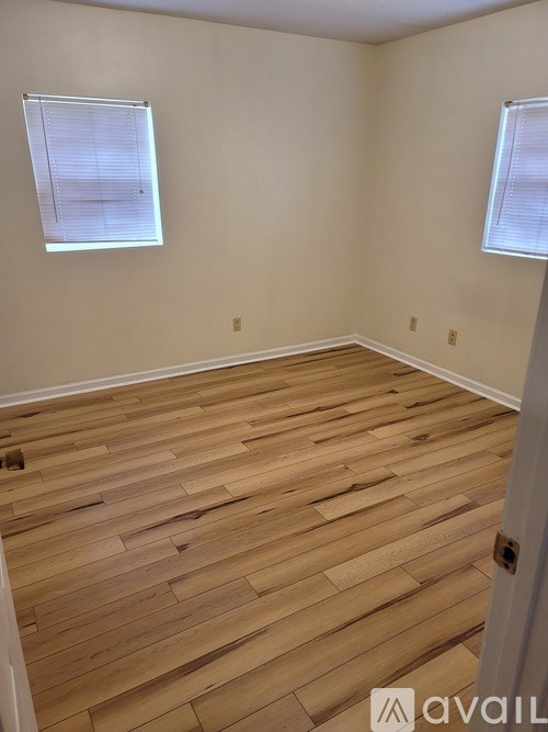 A room with wooden flooring and two windows.