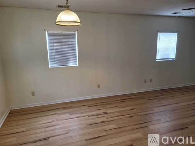 A room with wooden flooring and two windows with blinds.