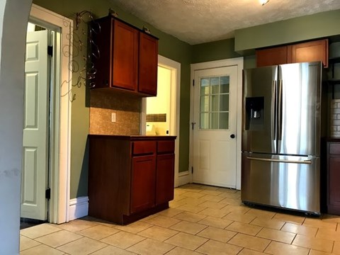 A kitchen with a refrigerator on the right and a counter with cabinets above it.