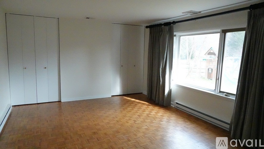 A room with wooden flooring and a large window with curtains.