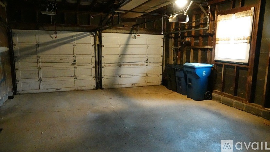 A large empty garage with a blue bin and a white door.
