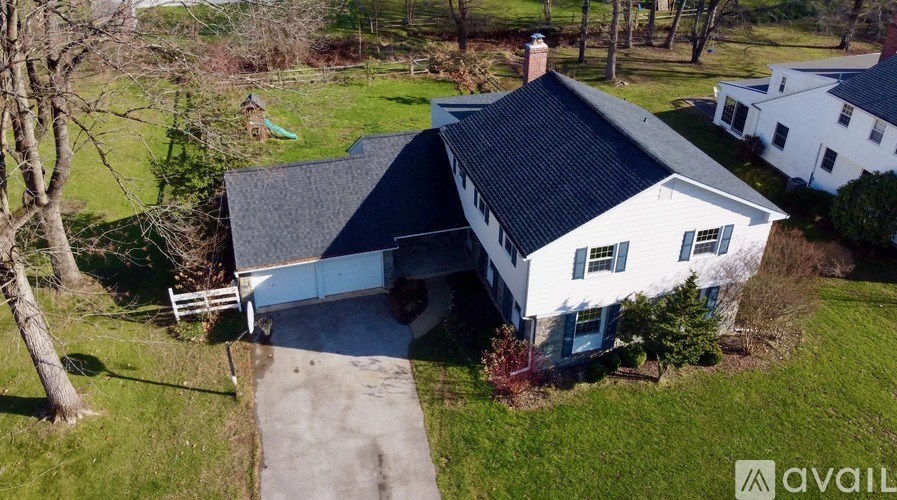 A white house with a black roof is surrounded by green grass and trees.