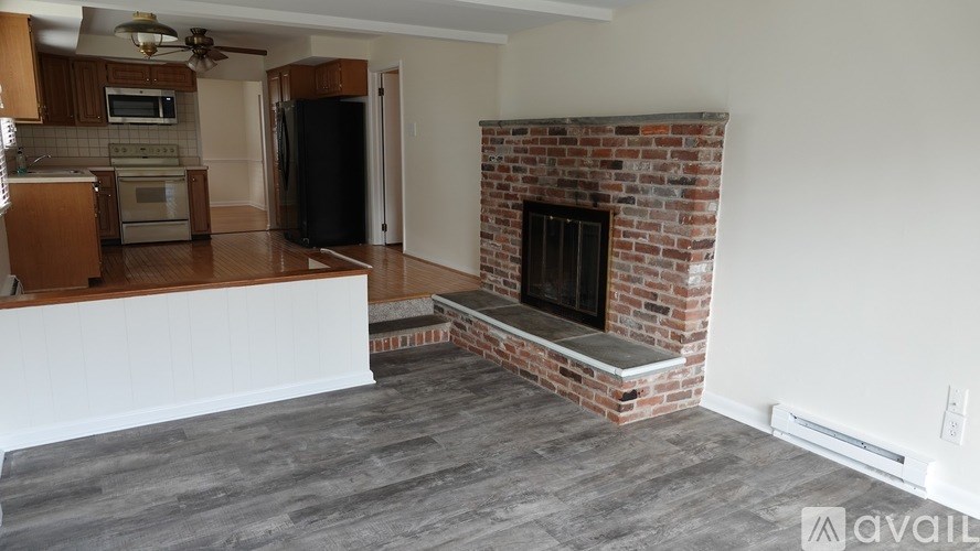 A living room with a brick fireplace and a kitchen area in the background.