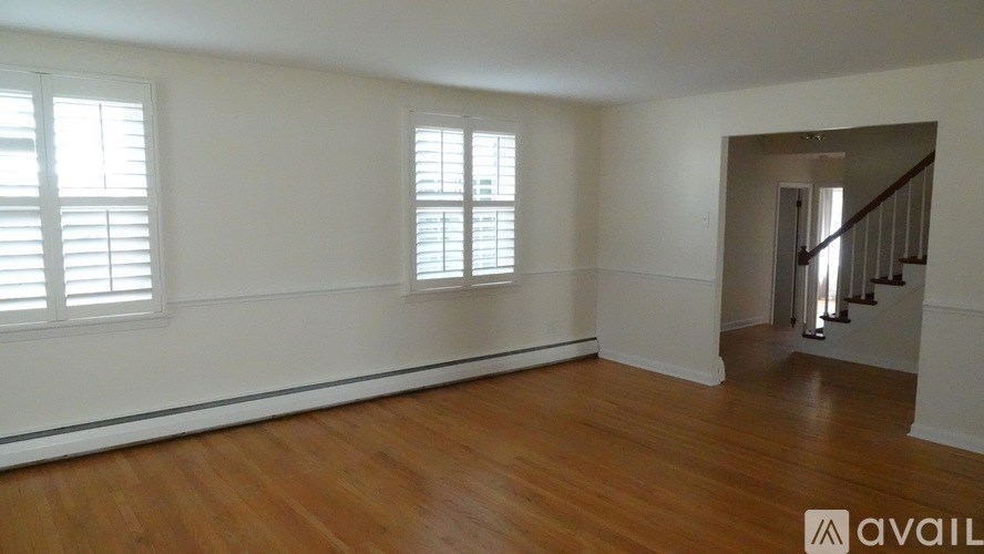 A room with wooden floors and white walls with a staircase in the background.