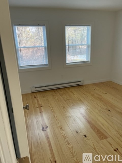 A room with wooden flooring and two windows.