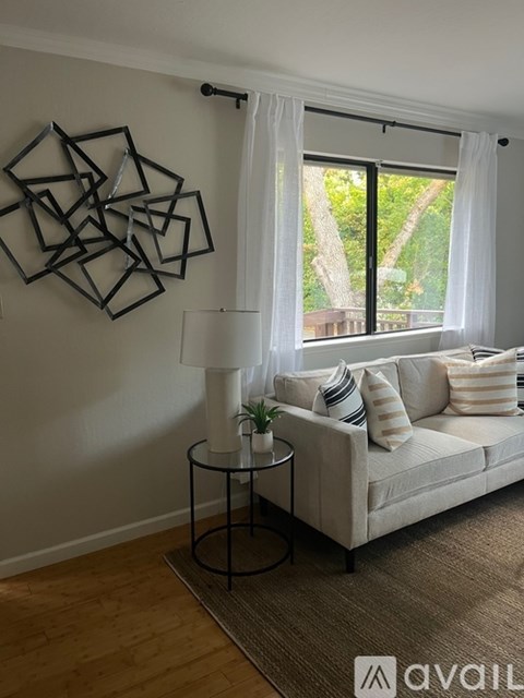 A living room with a white couch, a table with a lamp and a plant, and a wall art.