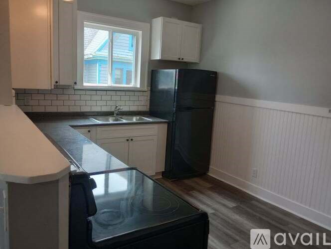 A kitchen with a black refrigerator and white cabinets.
