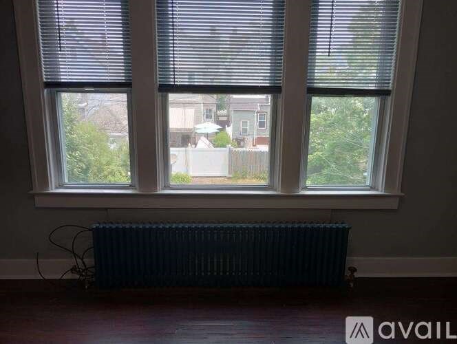 A room with a radiator and two windows overlooking a residential area.
