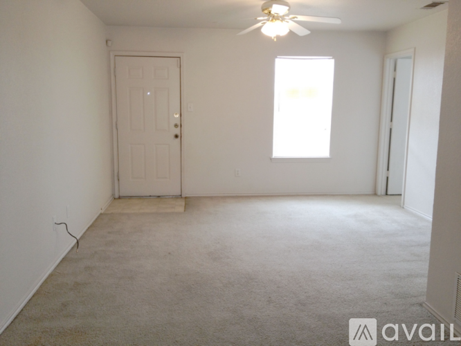 A room with a carpeted floor, a ceiling fan, and a door.