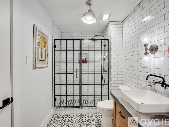A bathroom with a white sink, black and white tiles, and a black shower stall.