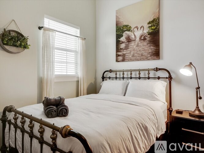 A bedroom with a large bed, a hanging plant, a window with curtains, and a painting of swans on the wall.