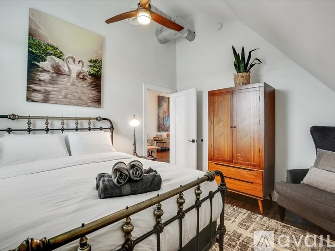 A bedroom with a bed, a ceiling fan, and a painting of swans on the wall.