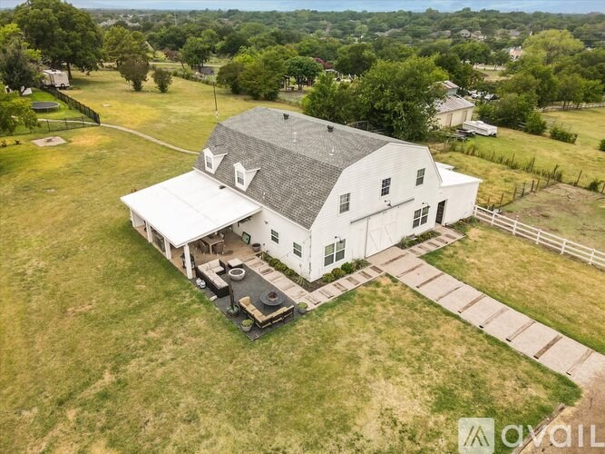 A white barn with a black roof and a black grill in the front yard.