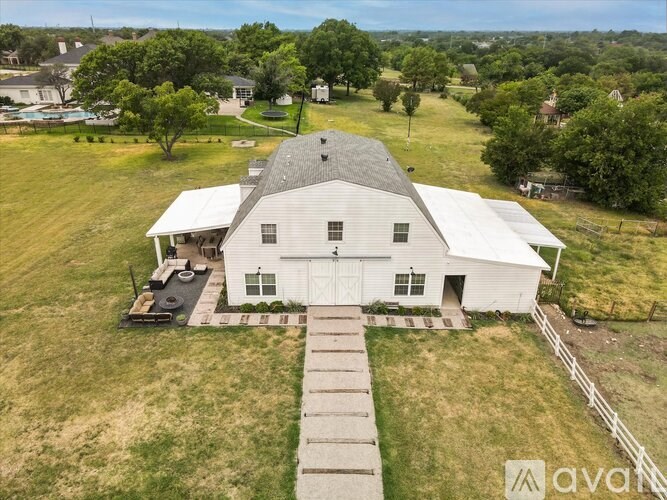 A large white barn with a grey roof is surrounded by a grassy field.