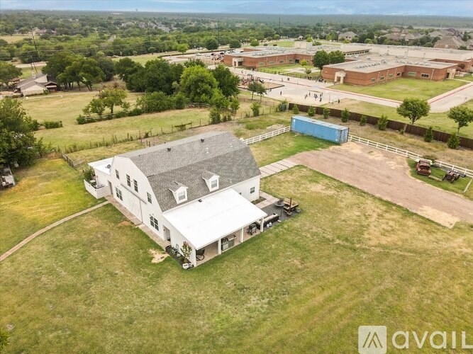 A large white house with a grey roof is surrounded by a grassy area and a fence.