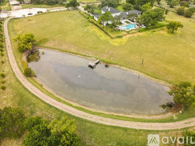 A bird's eye view of a pond surrounded by a grassy area and a house in the background.