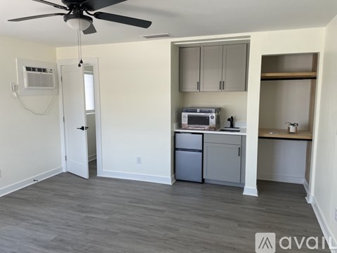 A room with a ceiling fan and a small kitchenette.