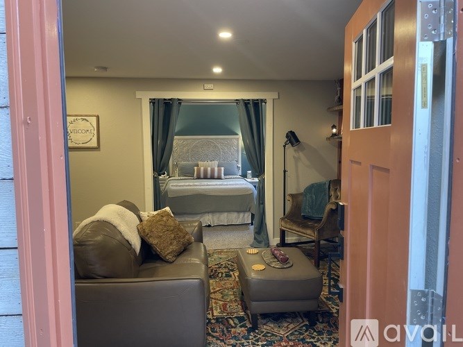 A living room with a grey couch and a bed in the background.