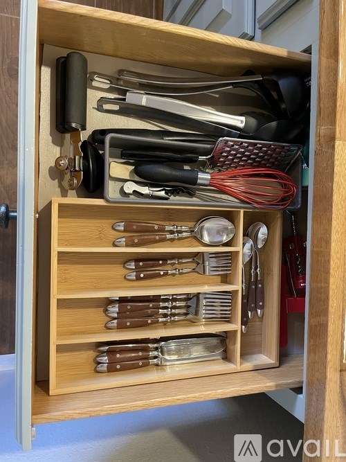 A kitchen drawer with utensils and a whisk.