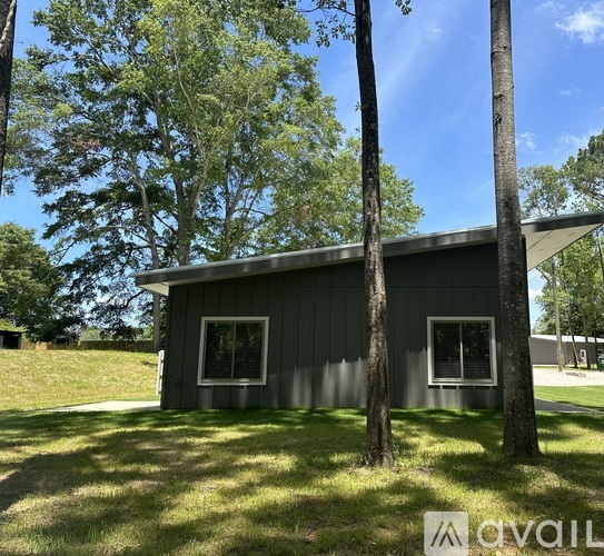 A small house with a grey roof and two windows is surrounded by trees.