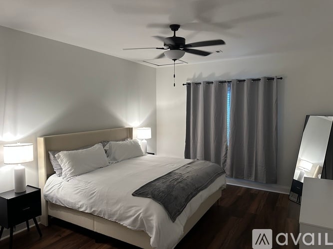 A bedroom with a large bed, a ceiling fan, and a nightstand with a lamp.