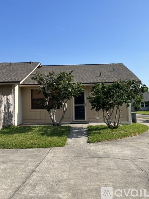 A house with a brown roof and a grey wall with a tree in front.