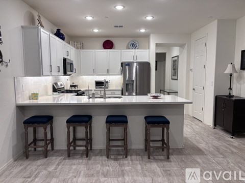 A kitchen with white cabinets and a white countertop with a bar stool in front of it.