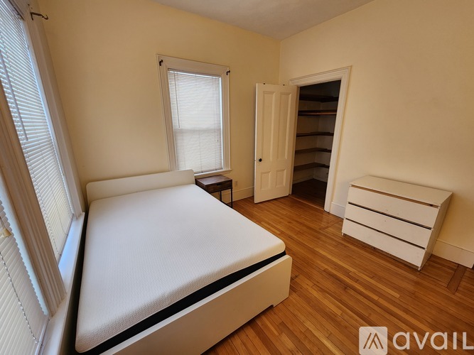 A bedroom with a bed, a window with blinds, and a wooden floor.