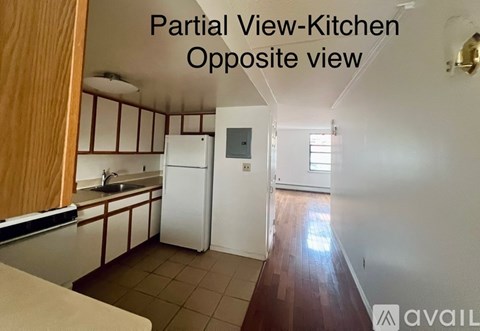 A kitchen with a refrigerator and a sink is shown from the opposite side of the room.