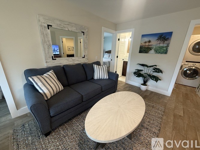 A living room with a grey couch, a round wooden table, and a mirror on the wall.