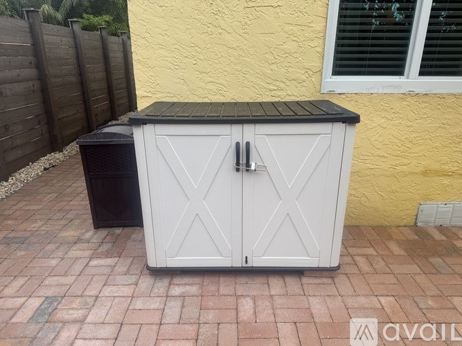A white cabinet with a black top is placed on a brick patio.