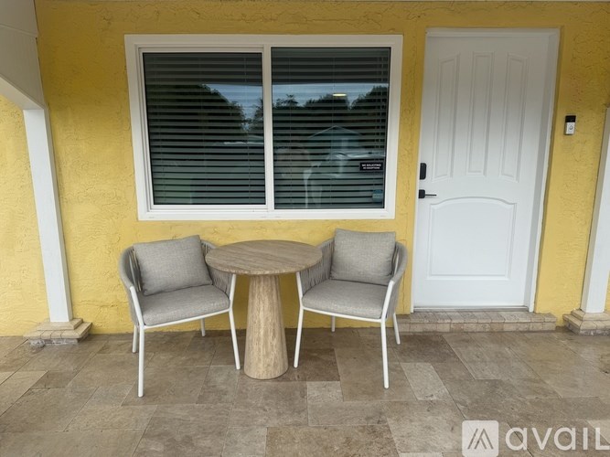 A table and two chairs are on a patio outside a yellow building.