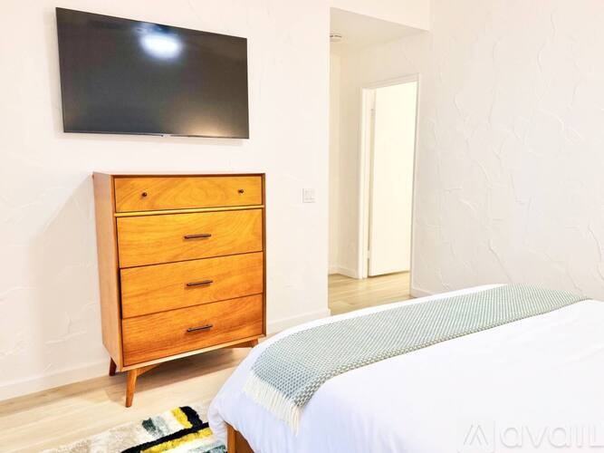 A bedroom with a bed, a dresser, and a flat screen TV mounted on the wall.