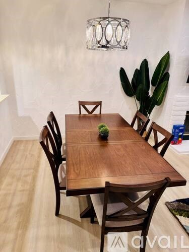 A wooden dining table with four chairs and a potted plant on the side.