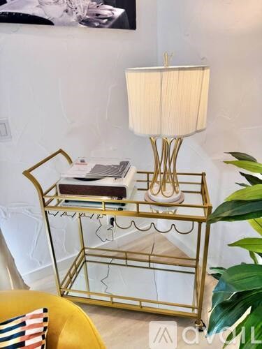 A gold lamp stand with a white lampshade and a book on it.