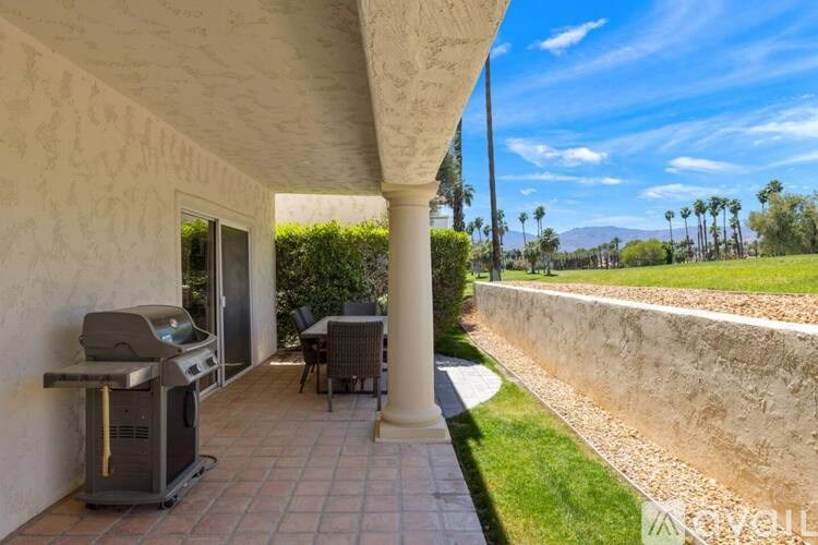 A patio with a grill and chairs overlooks a grassy area.