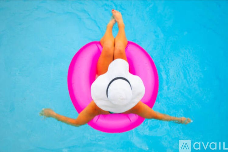A person in a white hat is floating on a pink inflatable ring in a pool.